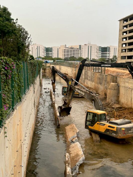 Excavator alongside a completed concrete retaining wall on a high-rise site