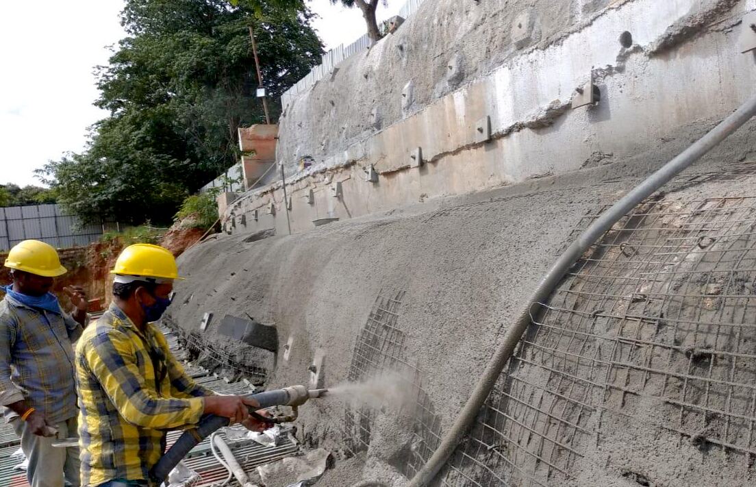 Workers applying shotcrete for soil nailing and slope stabilization on a retaining wall
